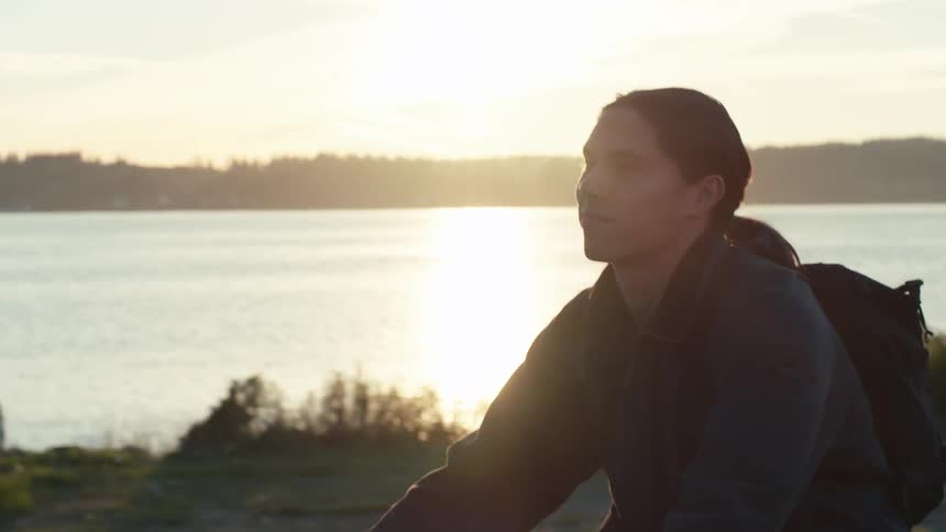 Young man riding a bike in a seaside setting with the sun on the horizon