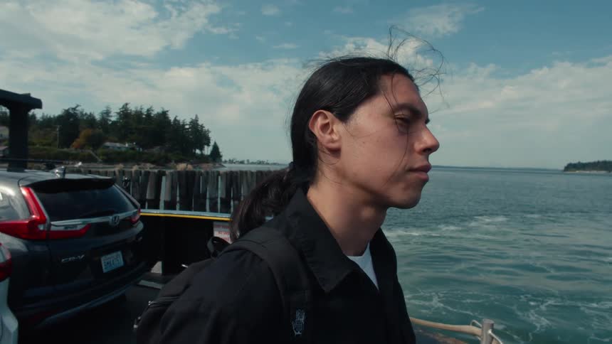 An indian teenager stands on a coast and sadly looks out to sea before walking away