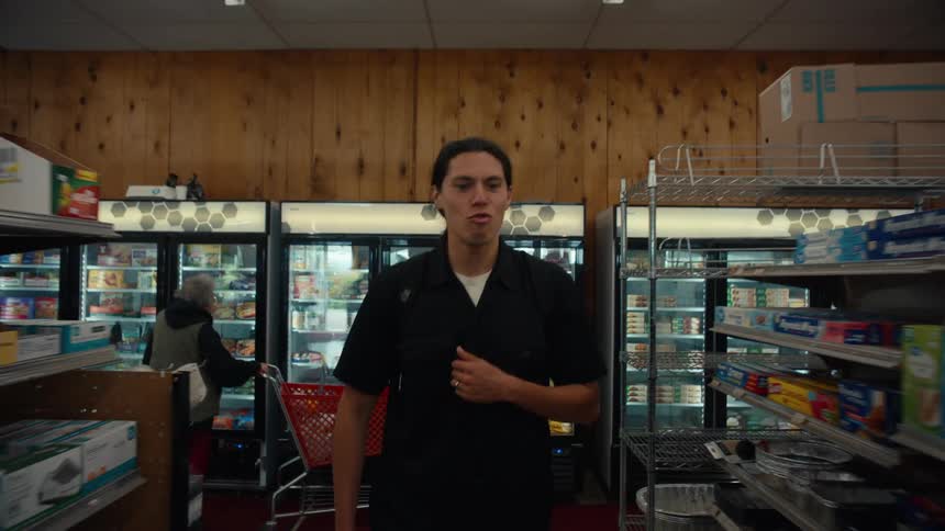 A young man in a black shirt is walking to a variety store and he is exchanging for something and then he stops and starts looking at the products