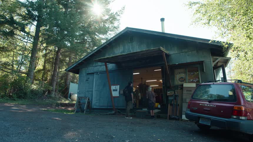 Two men talking outside a house in a setting surrounded by trees
