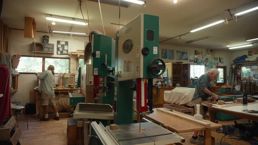 Two woodworkers are using tools in a well lit workshop focusing on woodworking projects