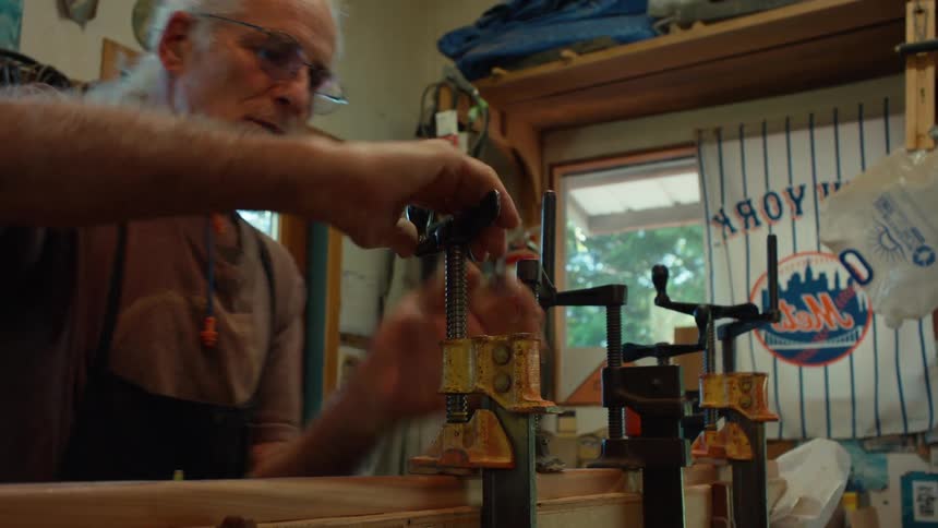 An elderly man is clamping a tool into a piece of wood and is turning the tool to make it stick tighter