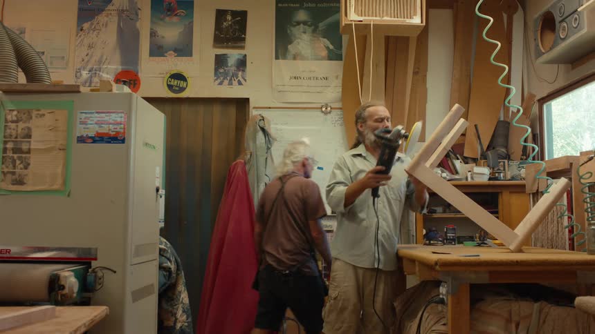 A woodworker meticulously sands a piece of wood with a power sander in a cluttered workshop