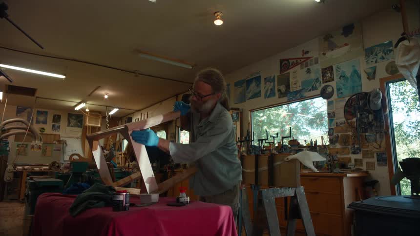 Carpenter wearing a glove applying a product to a wooden piece of furniture