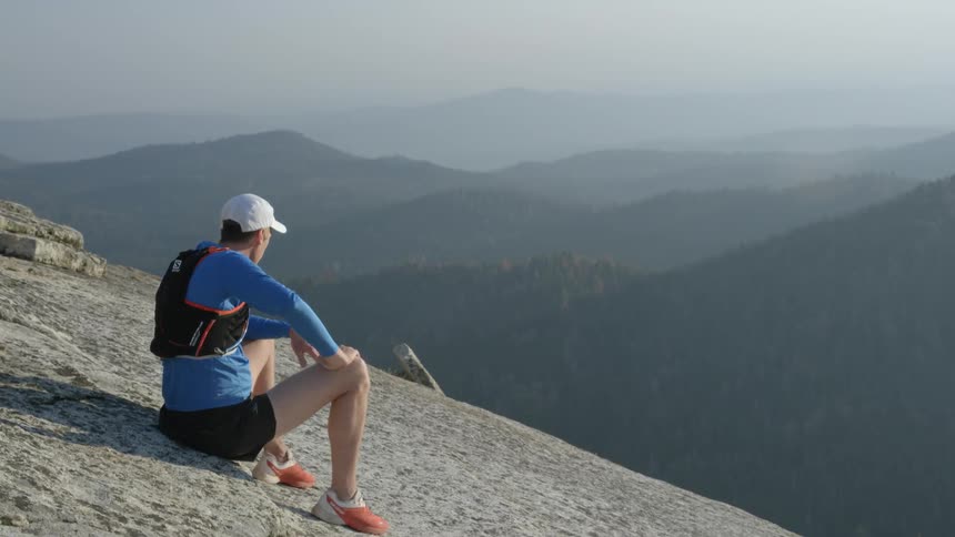 A man is sitting on a hillside looking out across a mountain range