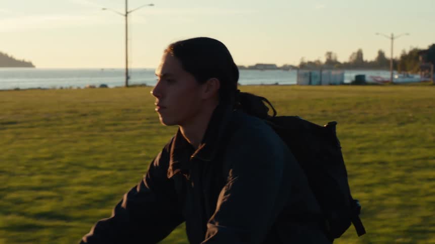 Man riding a bicycle on the edge of a field with the sea in the background