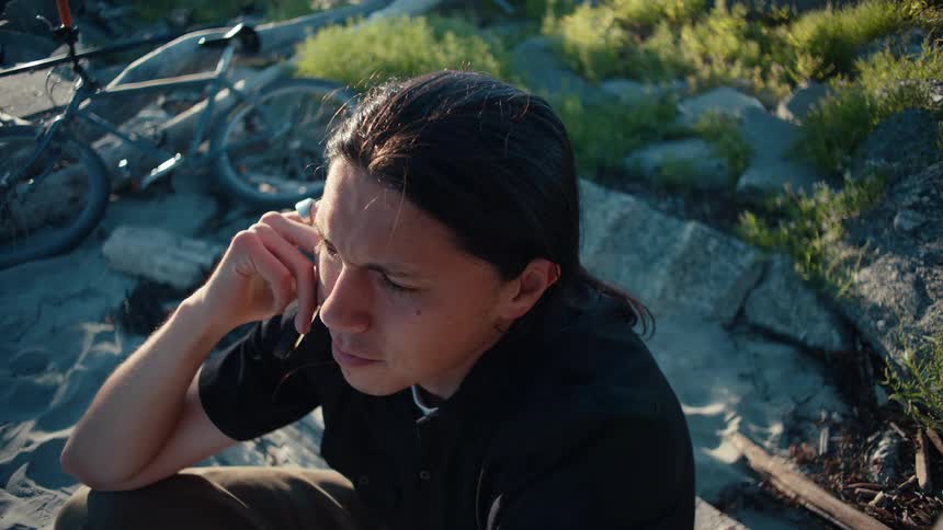Male sitting outdoors vaping in the wilderness while talking on a cellphone