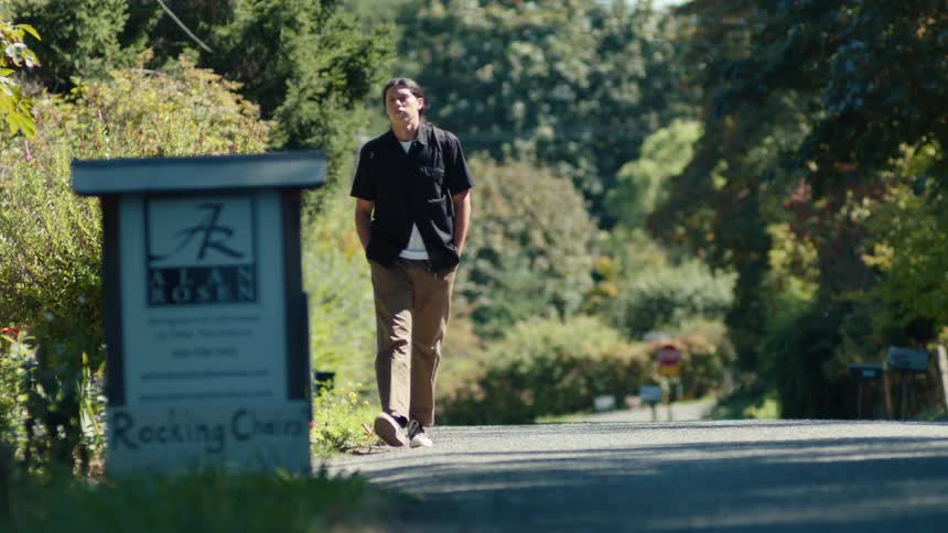A man walks down a country road past a roadside sign advertising rocking chairs by alan rosen