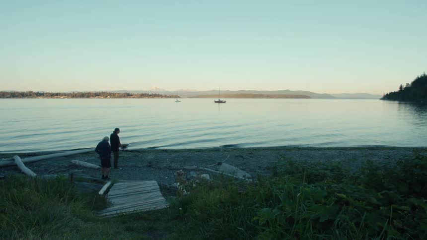 A dog runs past two men at the edge of the lake at dawn
