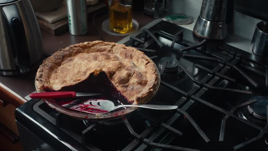 A fruit pie with a section removed sits on a stove in a kitchen