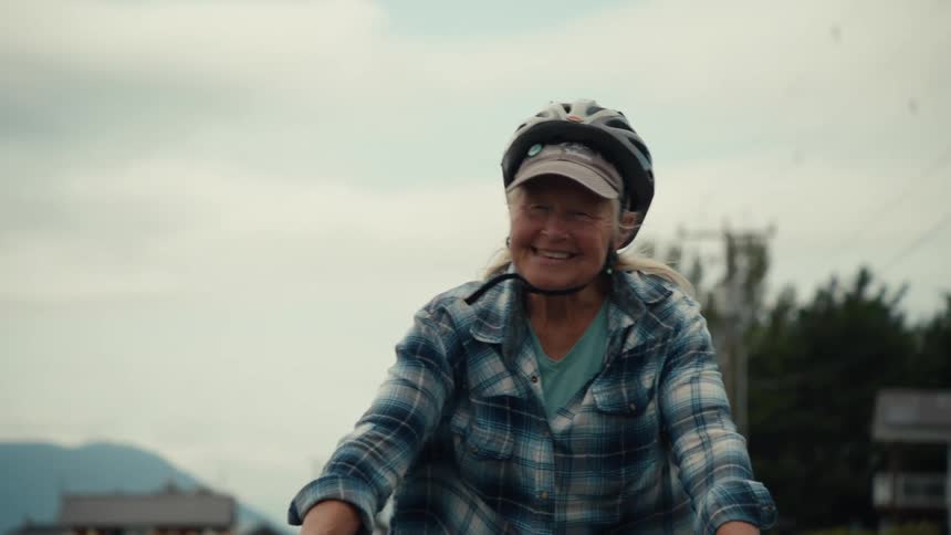 An elderly man and woman are riding bicycles on a cloudy summer day