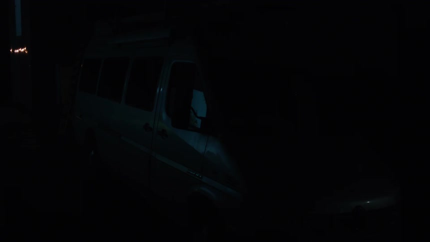 A large van parked in a dark empty lot the interior lights are on illuminating the interior