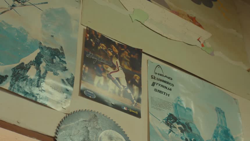 A collection of posters and a circular saw blade hang on a wall seemingly in a garage or workshop