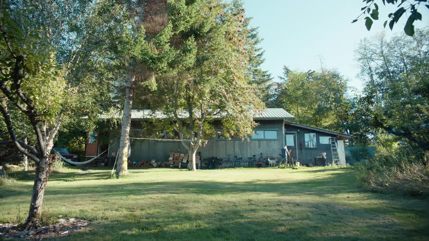 Man entering a house in the countryside with a large backyard with a dog running around