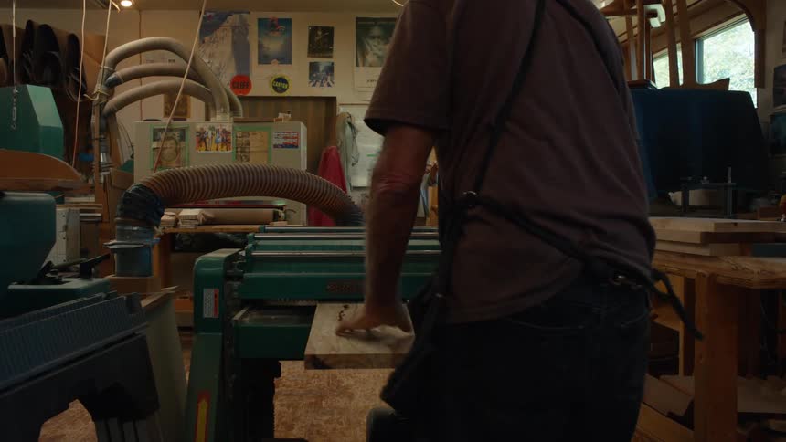 Two male carpenters in an indoor space with one of them operating a machine