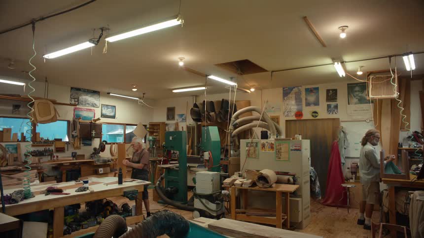 Two carpenter men are inside a workshop full of tools and are working on some objects