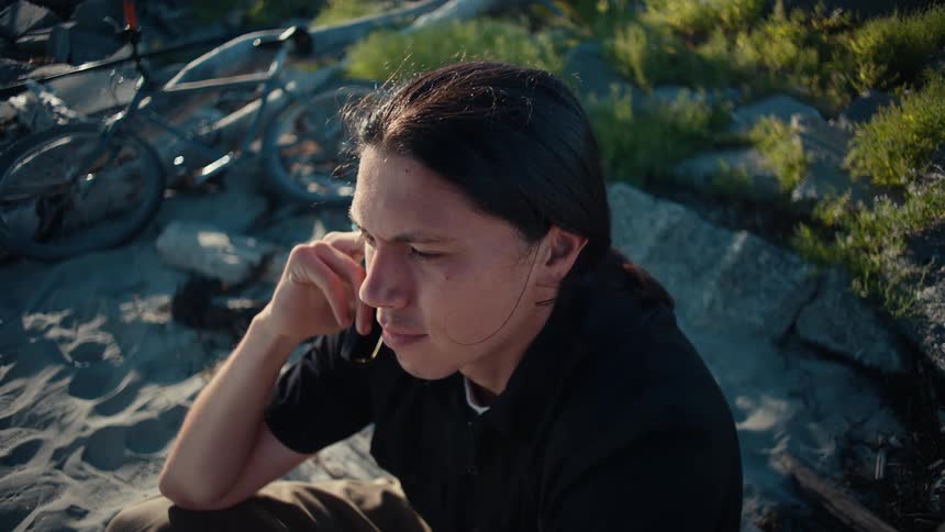 Young man sitting on the sand talking on his cell phone