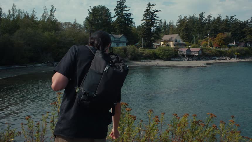 Man with backpack walking along the beach with houses in the background