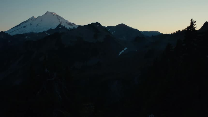 Pink tinted horizon contrasts with forested mountainous terrain during winter