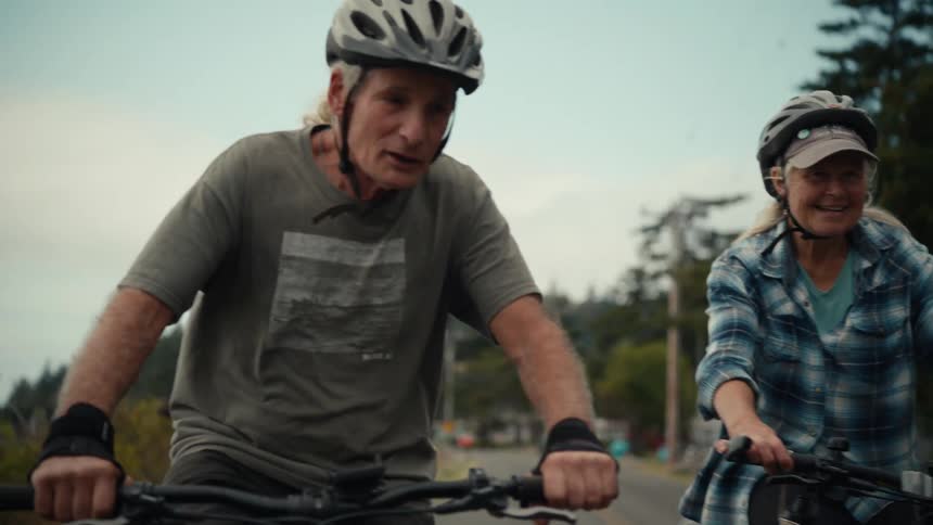 Elderly woman and man both wearing protective helmets riding a bicycle
