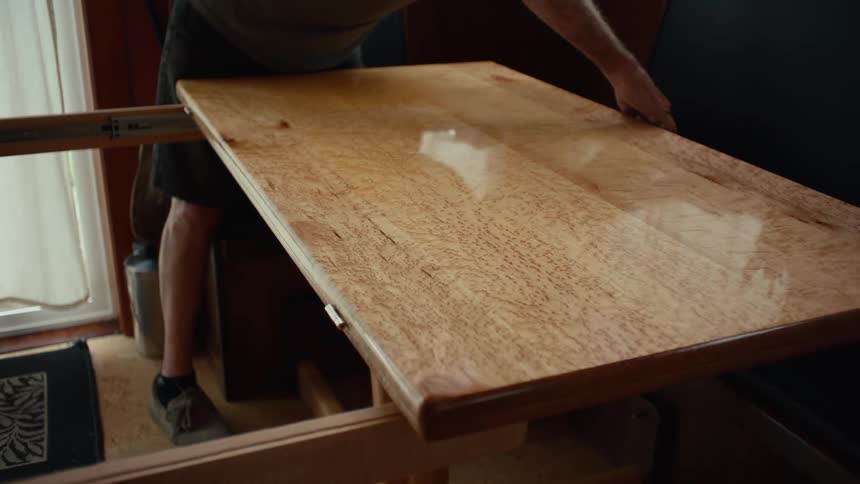 A person is opening a wooden table that is folded in half and its surface is shiny and smooth