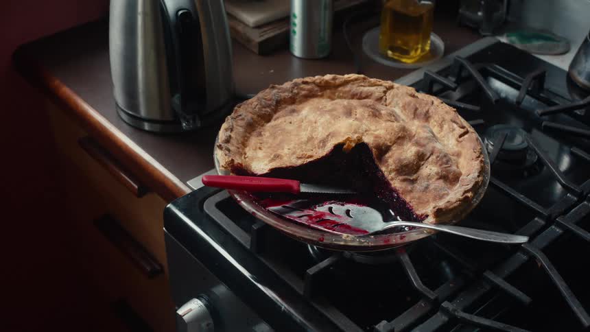 A freshly baked pie with a golden brown crust and a dark filling sitting on a stovetop with a knife and spatula nearby