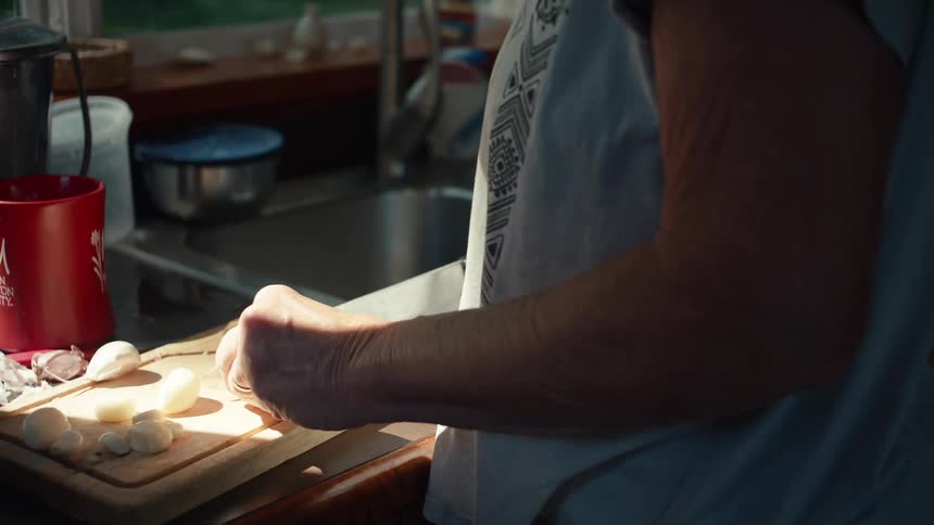 An elderly woman peels garlic cloves on a wooden cutting board