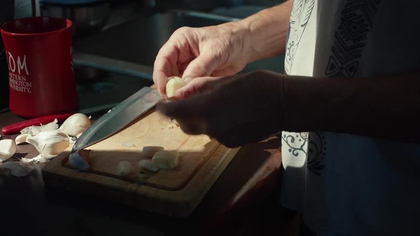 An adult chops garlic cloves on a wooden cutting board