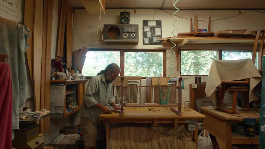 Carpenter sanding a wooden piece of furniture on a table