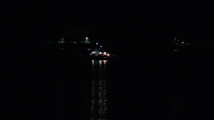 A boat sailing over a dark still body of water at night