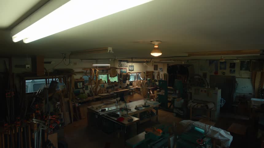 A cluttered woodworking workshop with tools and materials scattered across the workbenches as the lights flicker and begin to dim