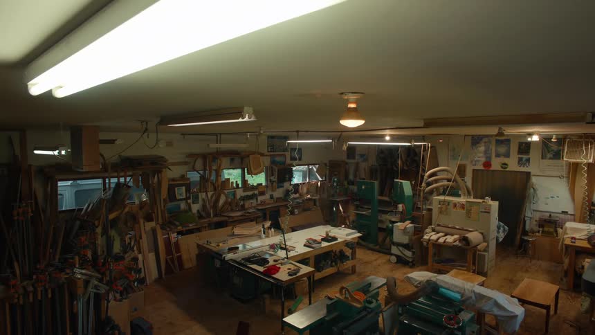 The inside of a workshop with several tools that is dark and then the ceiling lights are turned on