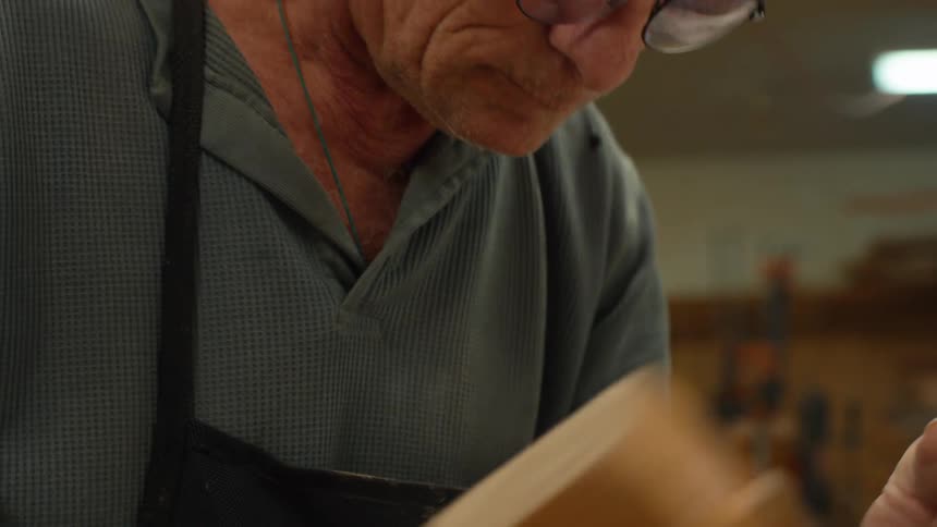 A person holds a wooden mallet and a chisel working on a piece of wood in a workshop