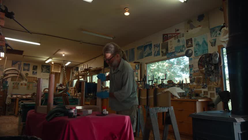 Carpenter with gloves applying varnish to a wooden object