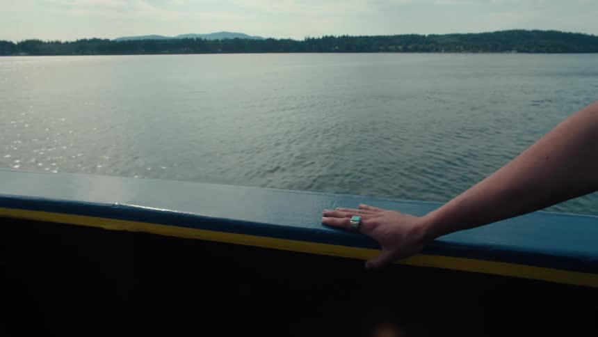 A boat is sailing on the water with a persons arm reached out bracing their hand on the side
