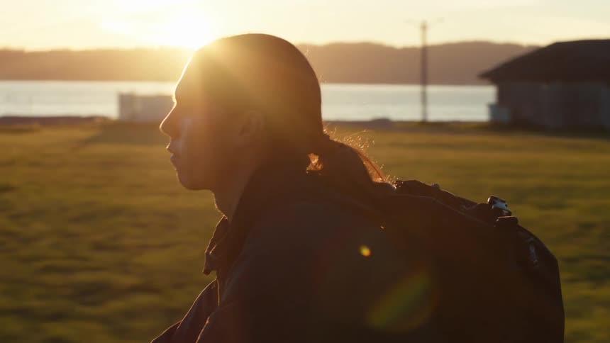 Side portrait of a man riding a bicycle on the edge of a lake with a reflection of the golden sun on the horizon