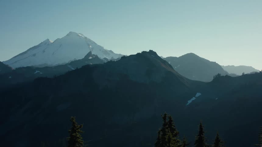 A snowcapped mountain stands tall against a clear blue sky surrounded by a range of dark rugged peaks