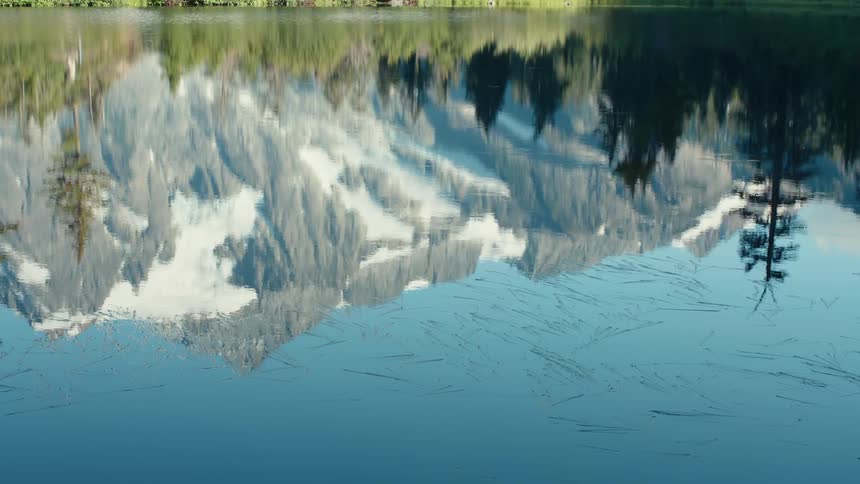 The surface of the water of a still lake that is reflecting a snowcapped mountain and some trees