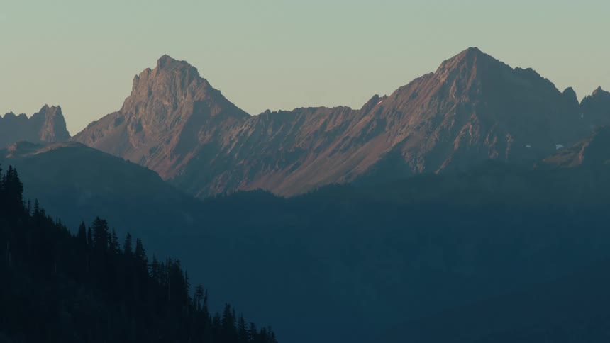 A majestic mountain range bathed in the warm glow of sunset with a hint of blue in the sky