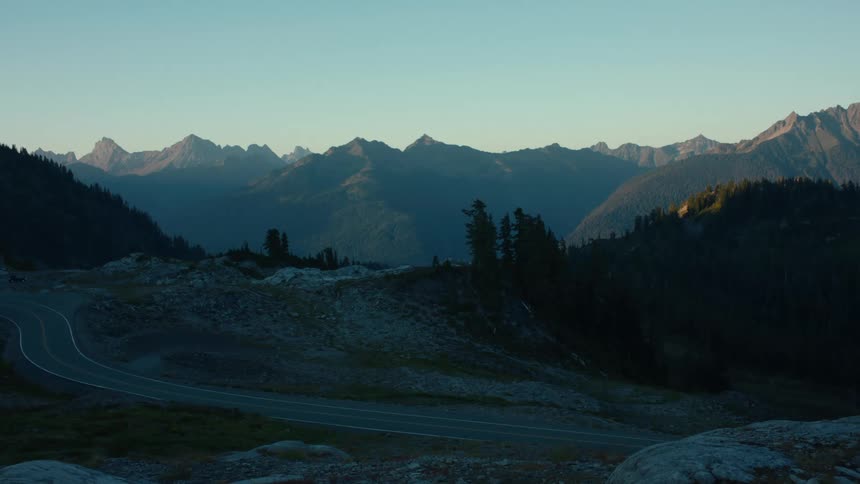 A winding road leads through a mountainous landscape during sunset