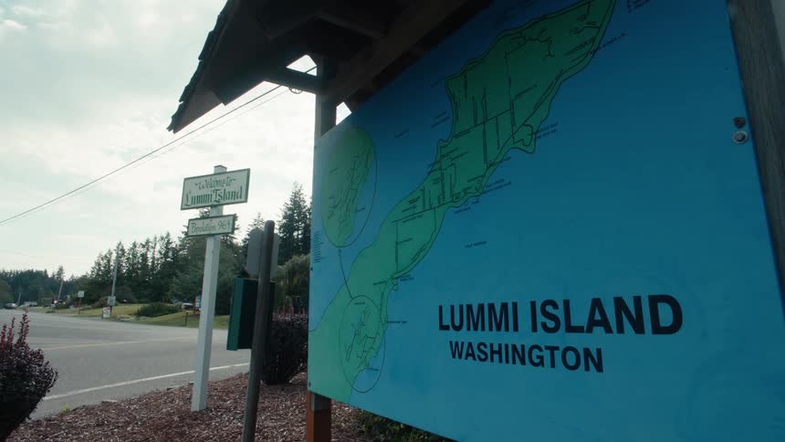 A large blue sign with a map of lummi island washington stands beside a road