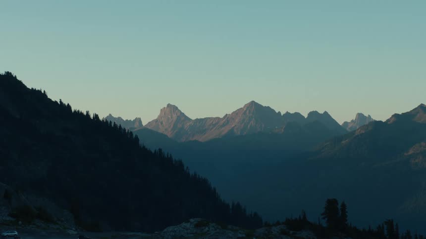 Cars sit parked near one of the forest covered mountains bracketing a foggy valley