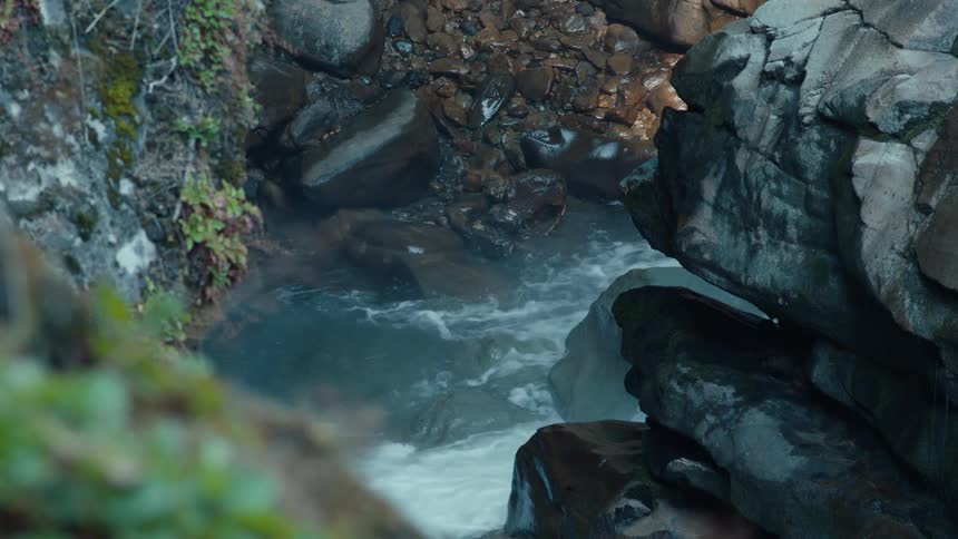 A rushing river flows through a narrow gorge surrounded by large rocks and lush greenery