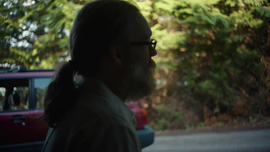The face of an adult man with a gray beard talking to a young boy standing to his right