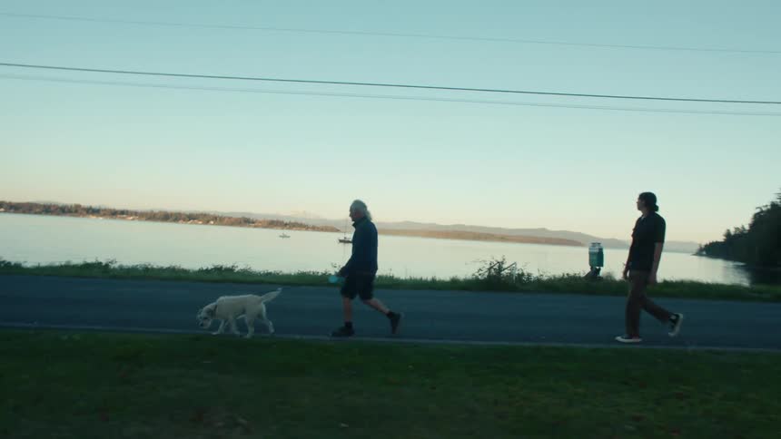 Two men walking with a dog on a paved area by the sea