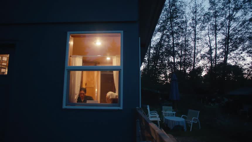 Exterior view of a house in the late afternoon and two people sitting in a room of the house