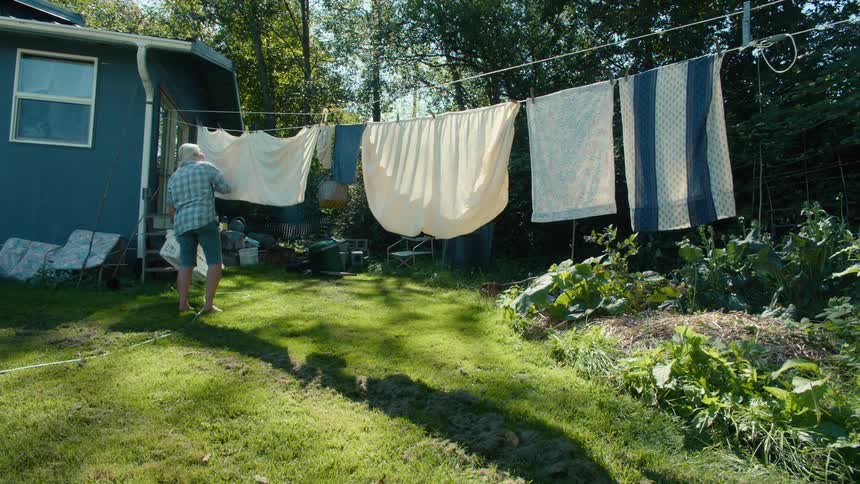 Older woman hanging sheets and towels to dry on a clothesline in the backyard