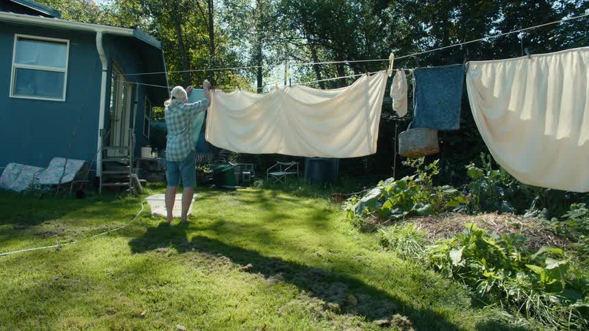 Older woman hanging sheets and towels on a clothesline in her backyard