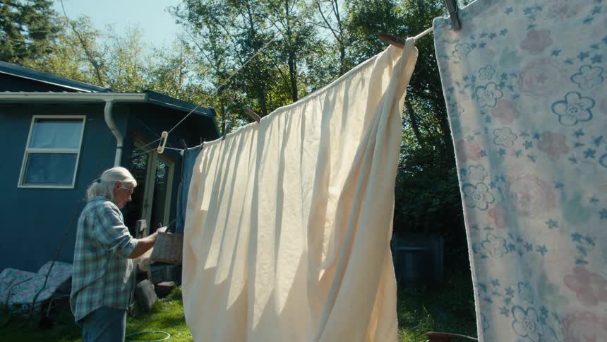 Older woman hanging sheets on a clothesline to dry on a sunny day