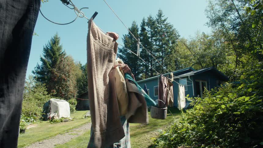 Older woman taking down towels from a clothesline in the backyard